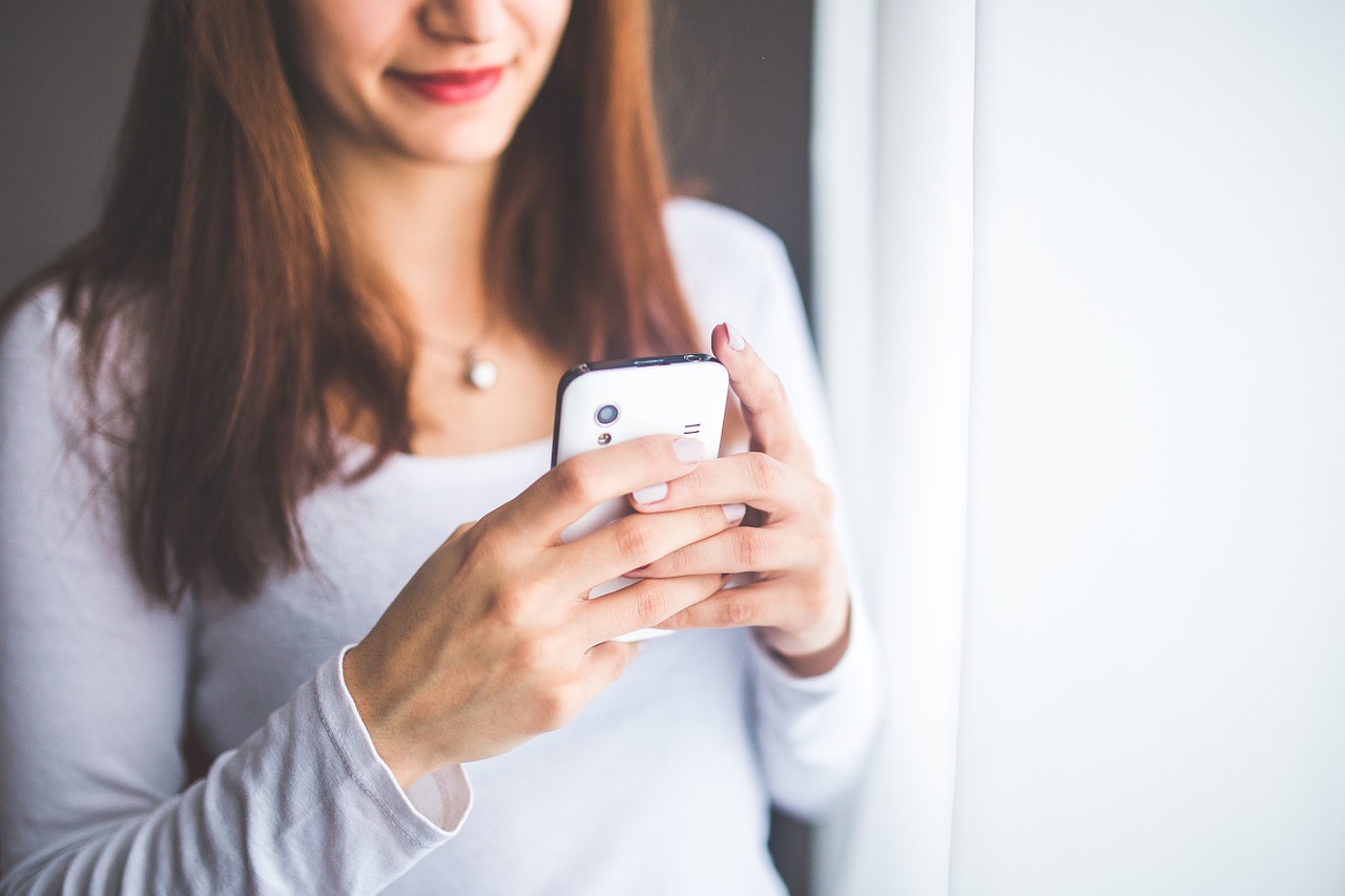 Junge Frau in der Schweiz nutzt ihr Smartphone. Bild zeigt Detailaufnahme von Händen, die ein Handy halten, mit Fokus auf moderne Technologie und Alltagskommunikation.