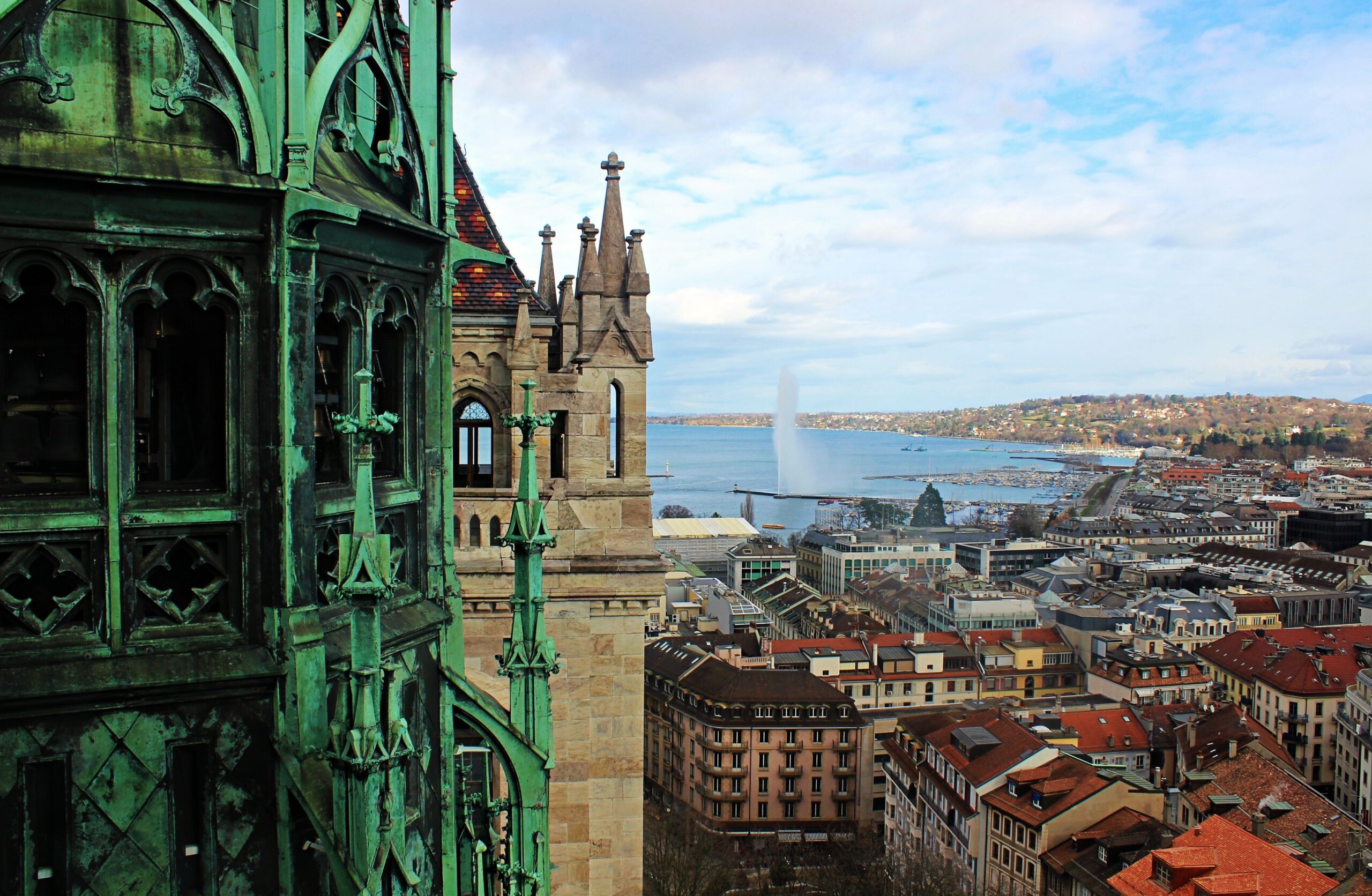 Blick auf die malerische Altstadt von Genf, Schweiz, mit dem berühmten Jet d'Eau im Hintergrund, aufgenommen von einem historischen Gebäude aus, der die reiche Kultur und Architektur der Stadt hervorhebt.
